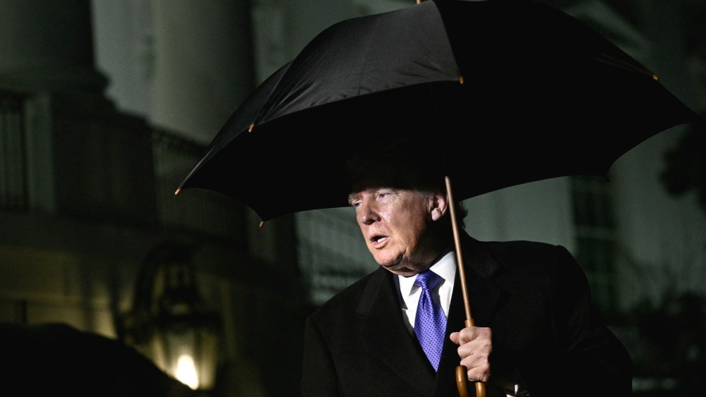 President Trumps walks out of White House at night, holding a black large umbrella.