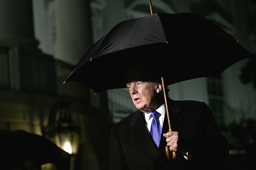 President Trumps walks out of White House at night, holding a black large umbrella.