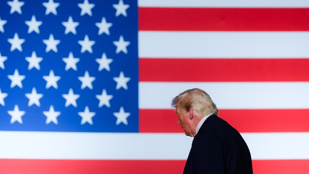 President Trump walks off stage. We see his profile in front an American flag backdrop.