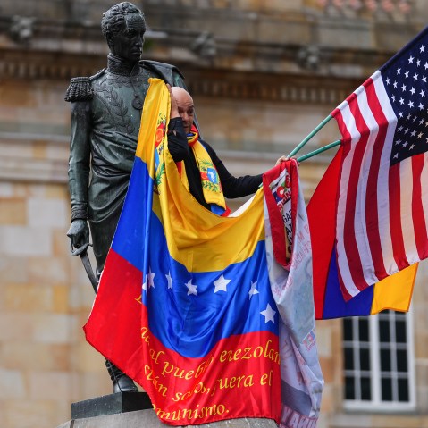 A man waves a venezuelan and american flag while standing a statue in Bogota.