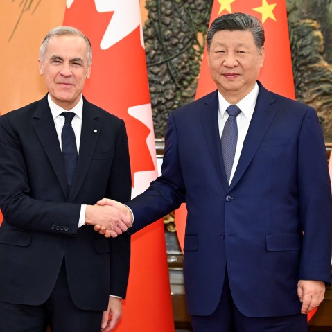 Canadian Prime Minister, left, and Chinese President shake hands as they pose for a portrait in front of the countries' flags.