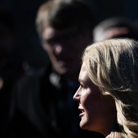 Press secretary Leavitt talks outside the White House, in a frame showing a very tight profile with members of the press in the background.