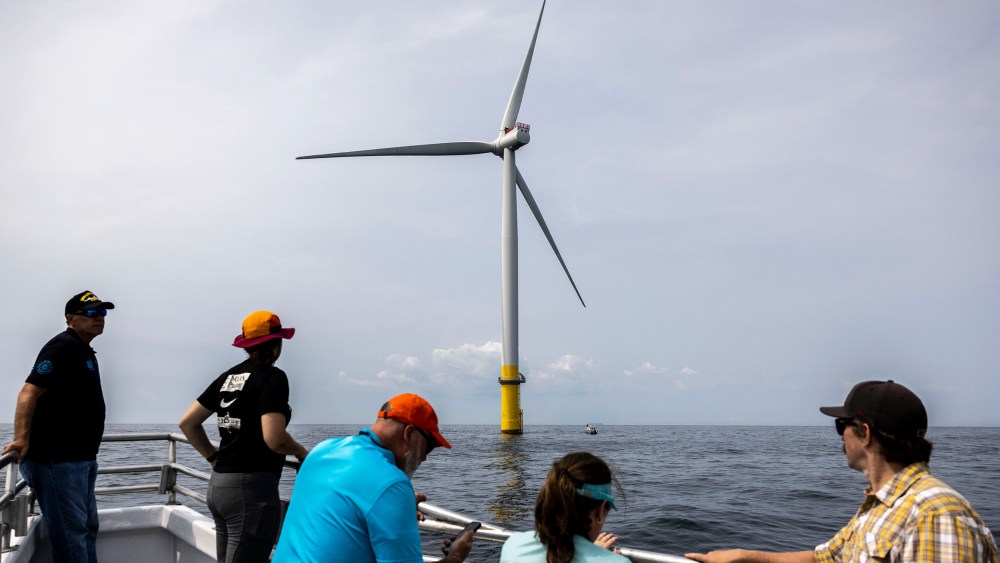 People look at a wind turbine in the water.