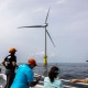 People look at a wind turbine in the water.