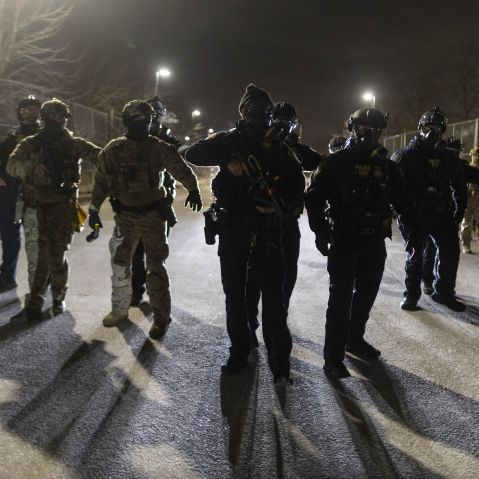 A line of ICE agents with guns drawn at nighttime.