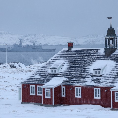 Greenland flag flies over building with Danish Navy ship in background