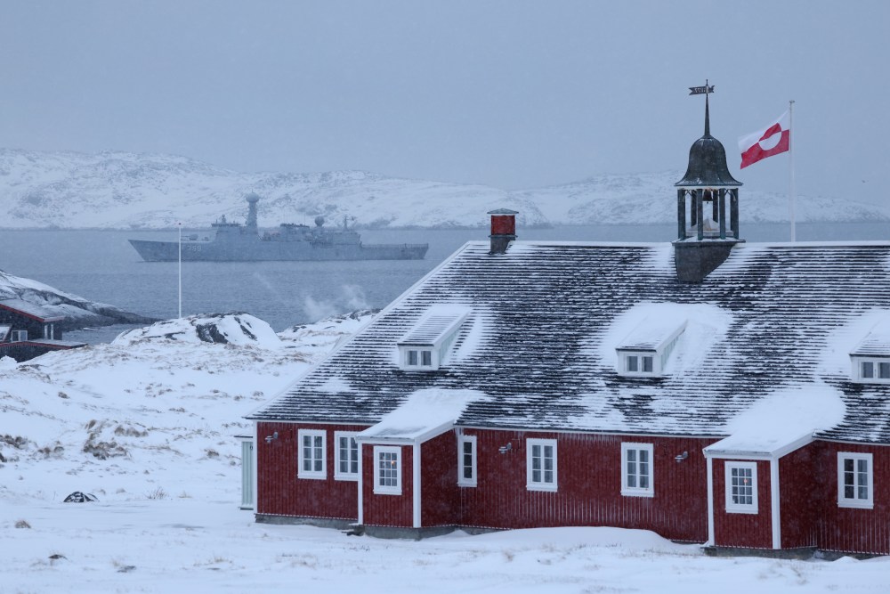Greenland flag flies over building with Danish Navy ship in background