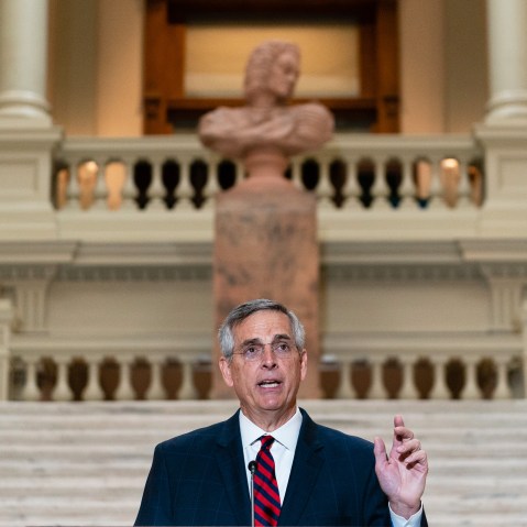 Brad Raffensperger speaks at the bottom of a staircase while gesturing with his hand.
