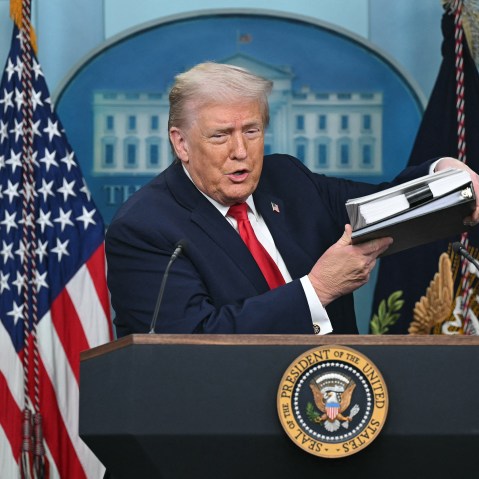 President Trump holds up a folder of documents as he speaks to the media during a briefing.