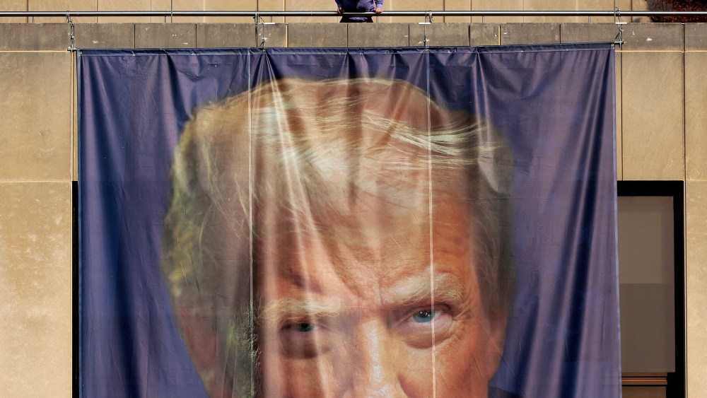 A person inspects a giant banner with the image of President Donald Trump hanging on the outside of the U.S. Department of Labor.