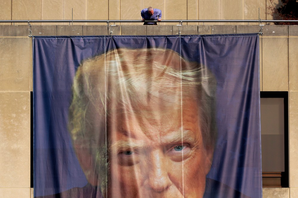 A person inspects a giant banner with the image of President Donald Trump hanging on the outside of the U.S. Department of Labor.